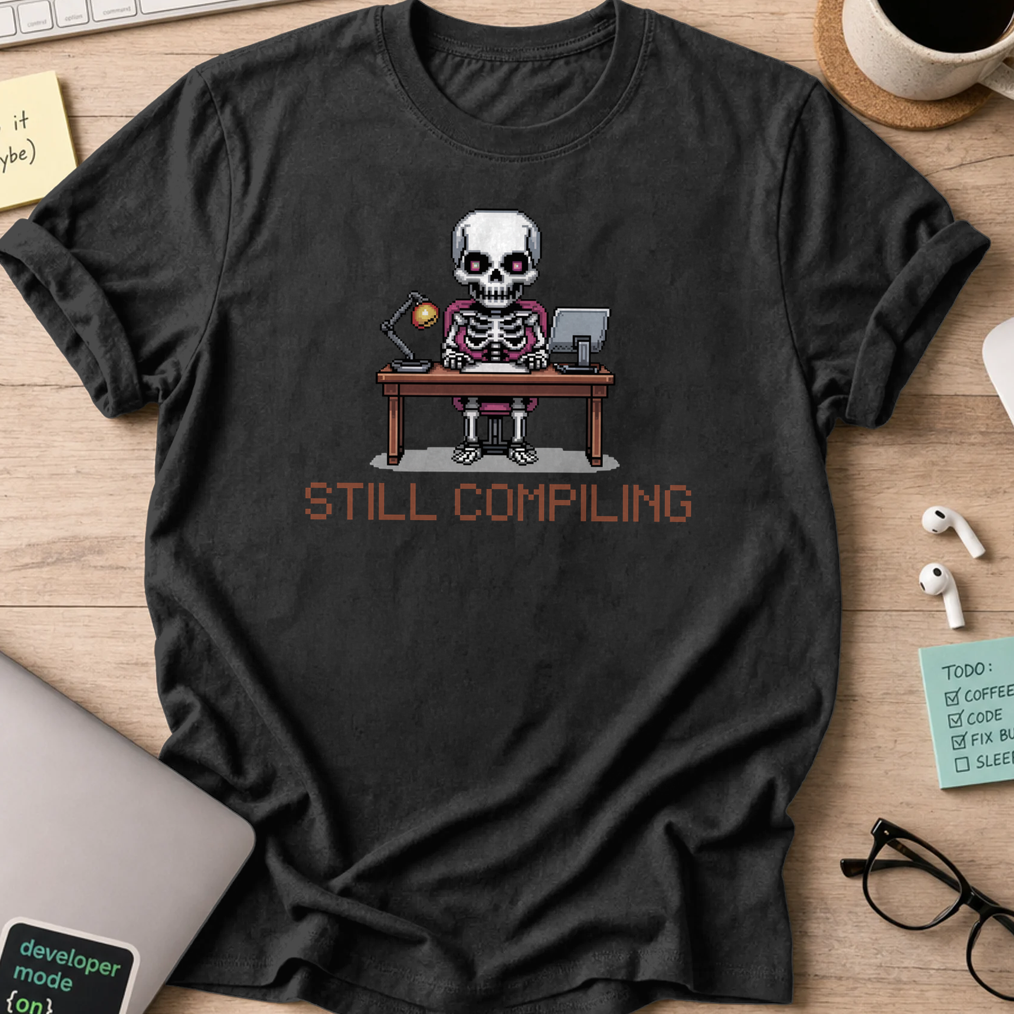 Black programmer shirt printed with "still compiling skeleton", a funny developer t-shirt and coding gift for software engineers and coders.